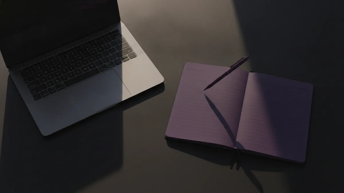 Notebook and pen near a laptop to plan bio link text and destinations
