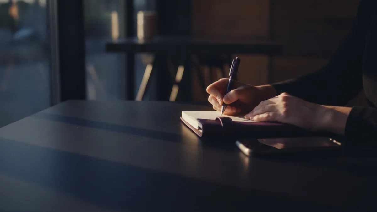 Authentic voice drafting Writing a personal bio draft with a notebook at a cafe table
